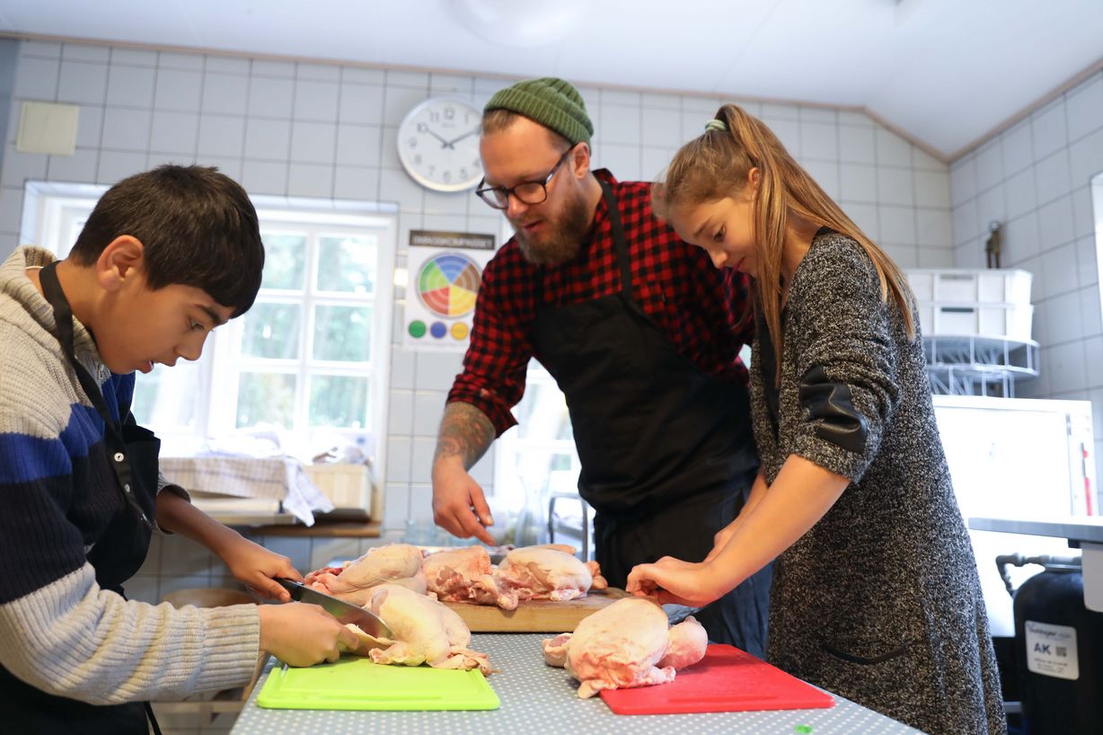 Anees (tv.) er sammen med Milica (th.) i køkkenet for at forberede aftenens festmenu. Kokken Martin 'Guf' Becker vejleder eleverne i korrekt udskæring af kyllingerne. Foto: Jan Klint Poulsen Anees (tv.) er sammen med Milica (th.) i køkkenet for at forberede aftenens festmenu. Kokken Martin 'Guf' Becker vejleder eleverne i korrekt udskæring af kyllingerne. Foto: Jan Klint Poulsen